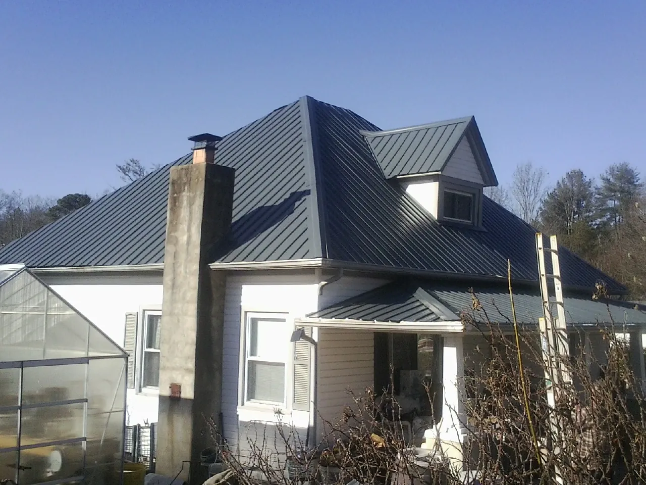 Dark blue standing seam metal roof on a white farmhouse with dormer — Slate & Tile Roof Repair by Roofing Brothers in Cliffside