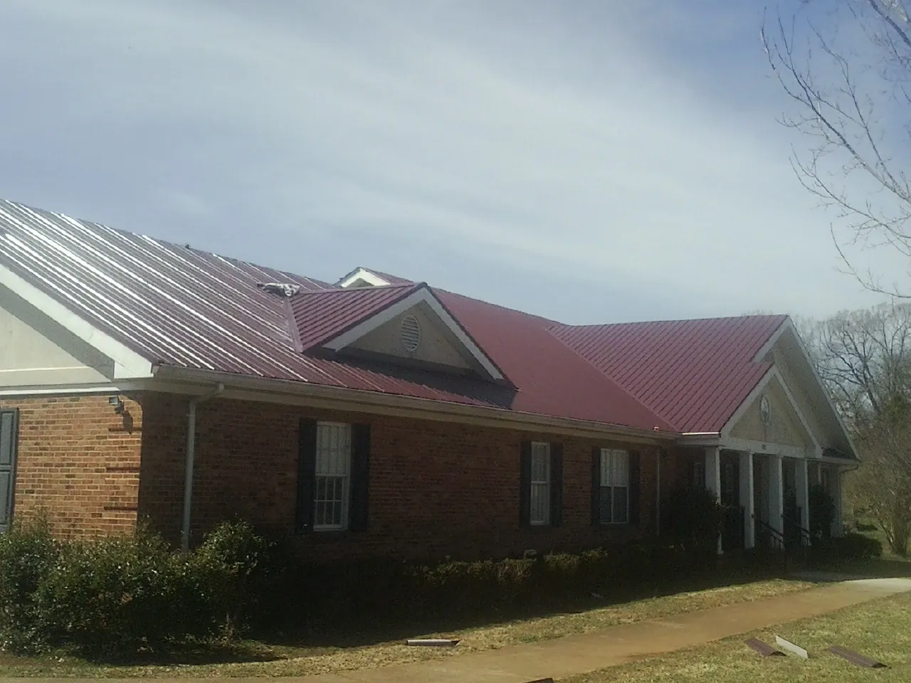 Red metal roof with gabled entries on a long brick building, from a Hail Damage Roof Repair job in Cliffside