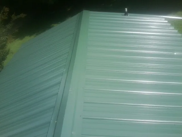 New green metal panels meeting at the ridge of a roof — Flat Roof Repair work by our crew in Cliffside