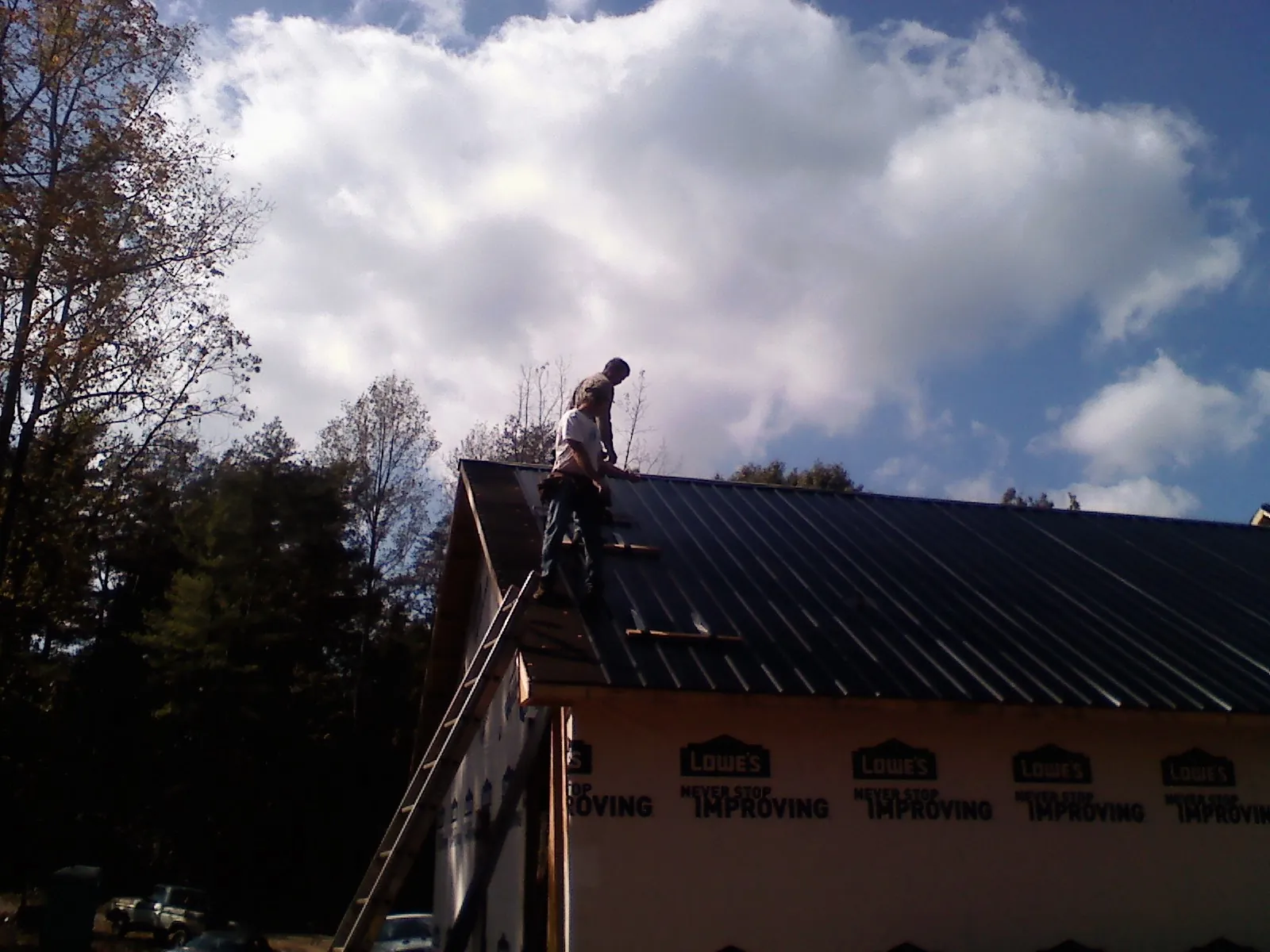 Roofer fastening dark metal panels high against a cloudy sky, from a Roof Inspection job in Cliffside