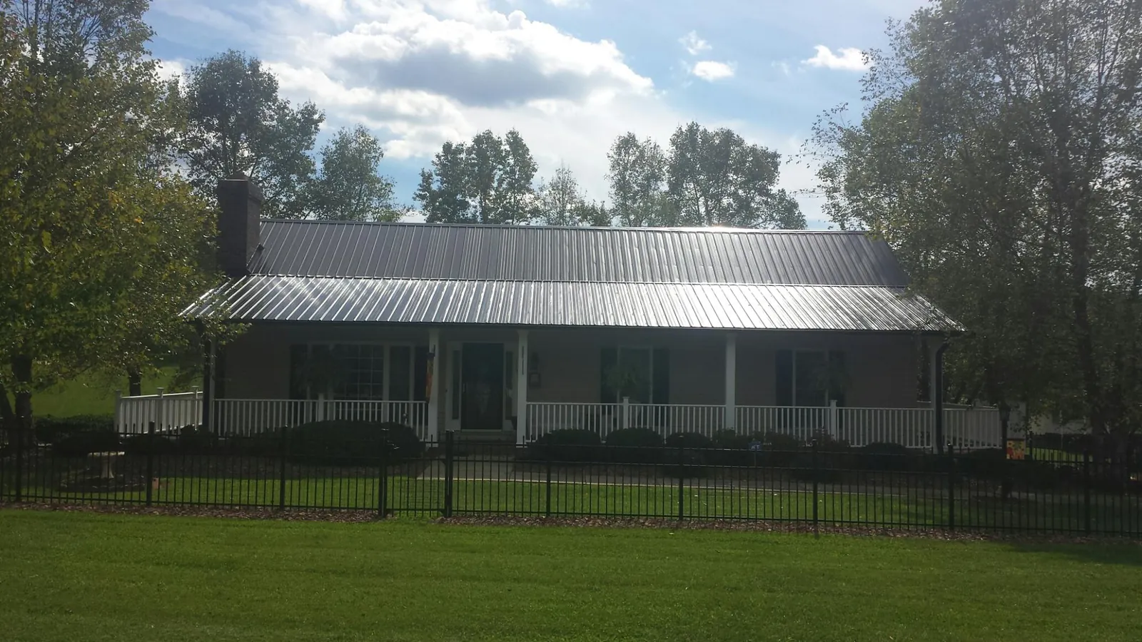 Gray metal roof on a brick ranch with a full width front porch — Gutter Guard Installation work by our crew in Cliffside